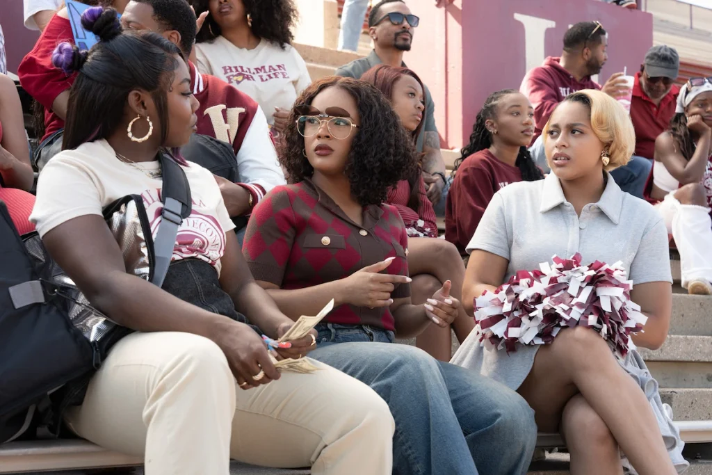 Rashida, Deborah, and Hazel sit among spectators wearing Hillman colors in A Different World