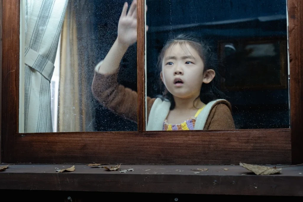 Wen raises a hand against a cabin window in Knock at the Cabin