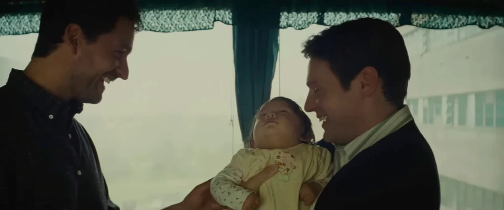 Two men smile at a baby held between them in the official Knock at the Cabin trailer