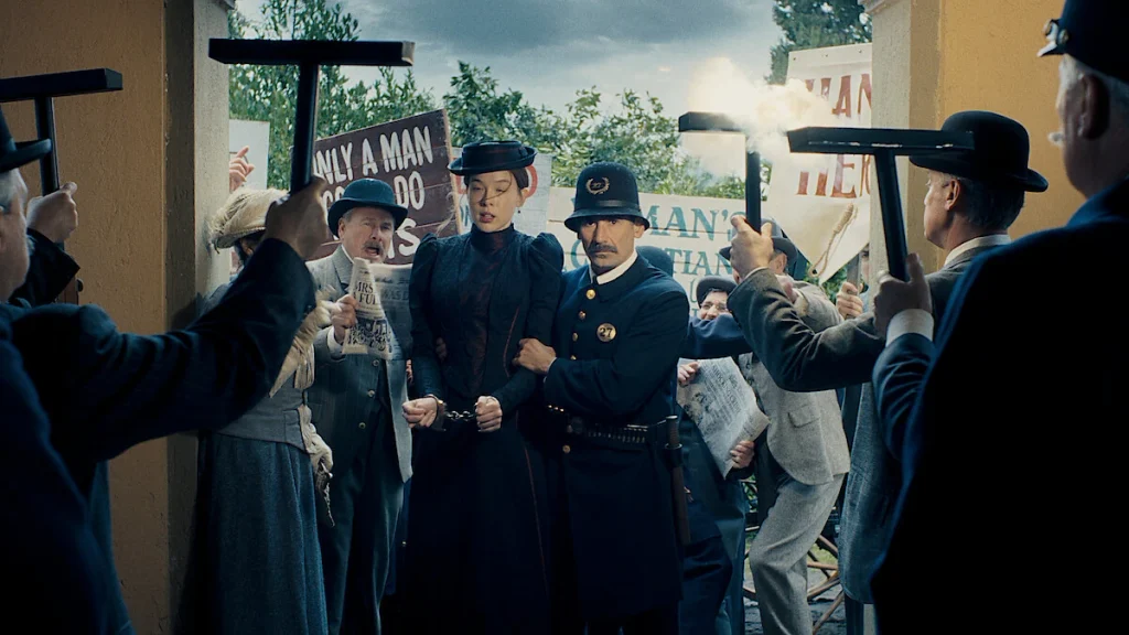 Lizzie Borden is escorted through a crowd by a uniformed officer in Netflix's Monster