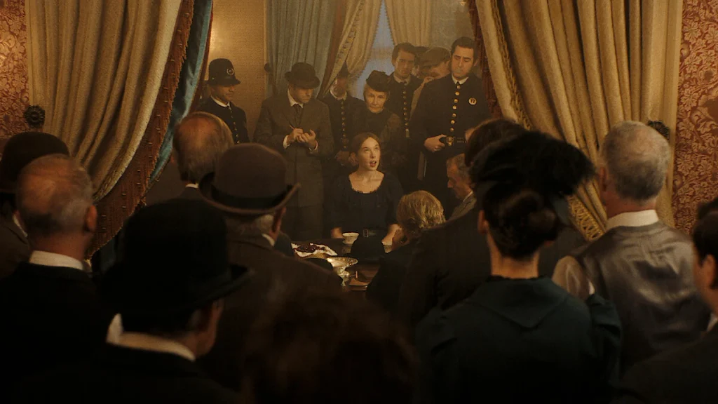 Lizzie Borden sits at a table surrounded by officers and other visitors in a scene from Monster
