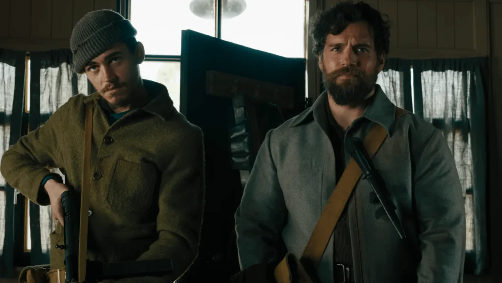 Two armed men in heavy coats standing in a dim interior beside a bright window