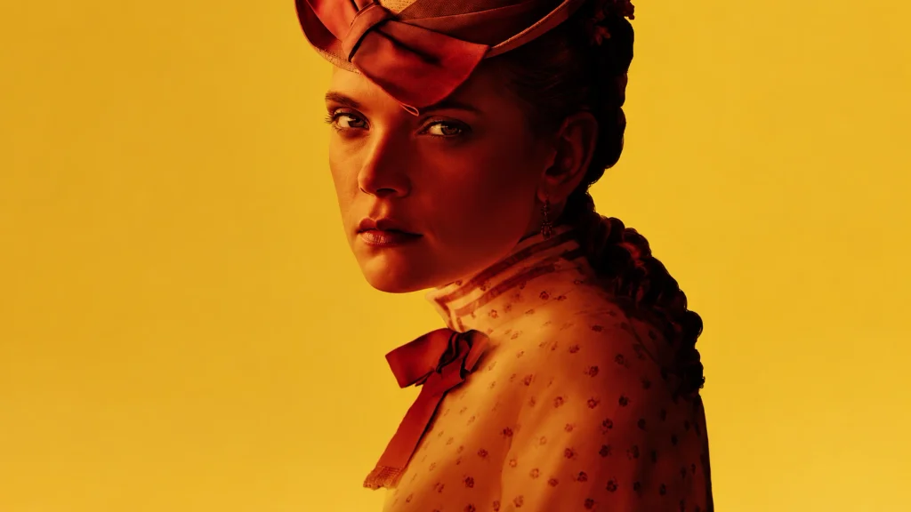 A woman in period dress looks toward the camera against an amber background in The Doll