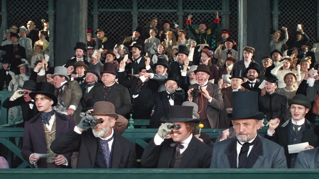 A large crowd in formal period clothing watches a horse race in The Doll 