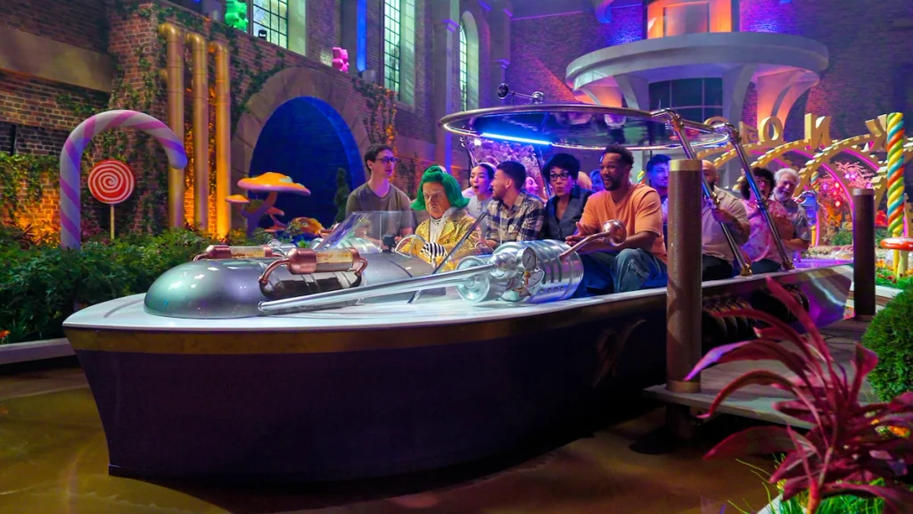 Contestants ride a silver boat past giant candy decorations inside the factory in Wonka's The Golden Ticket