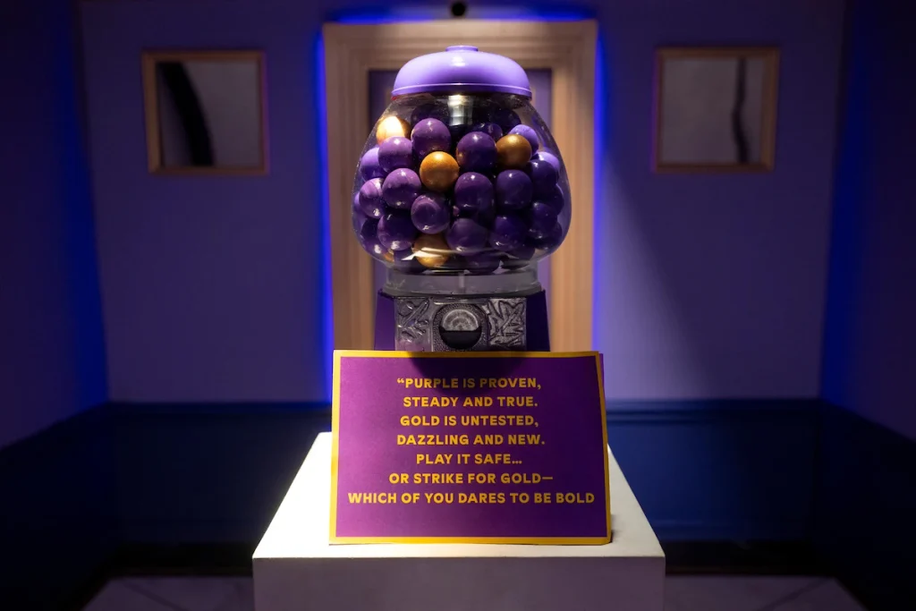 Purple and gold gumballs sit above a sign offering a safe choice or a risk in Wonka's The Golden Ticket