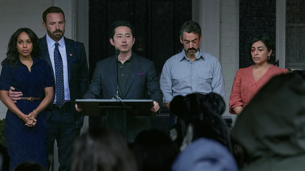 Sam speaks at a microphone while Mark, Abigail, Ramon, and Cecilia stand beside him.