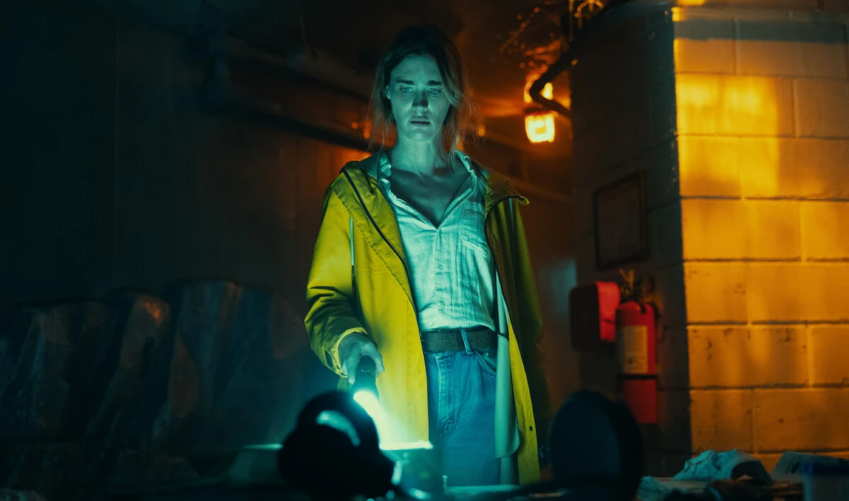 Fonda Howander holds a flashlight in a dim room, wearing a yellow raincoat.