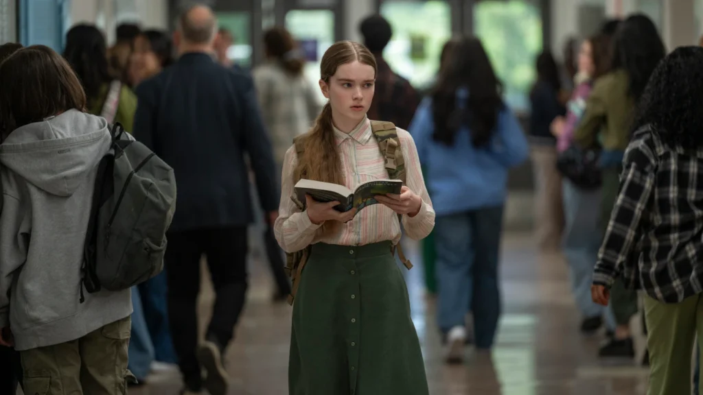Carrie holds an open book in a crowded school hallway.