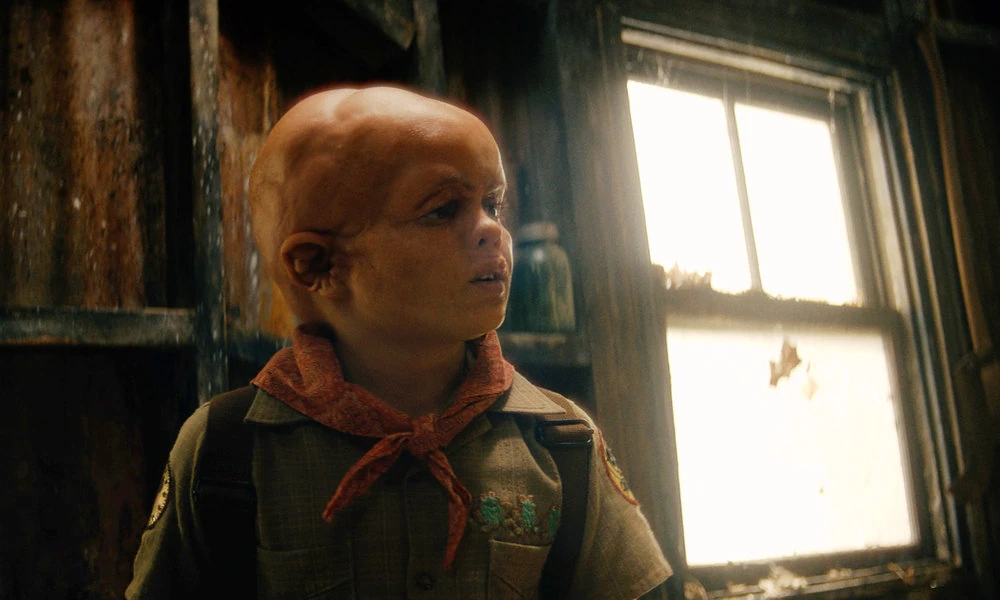 Young Jason stands beside a window, wearing a camp uniform and red neckerchief.