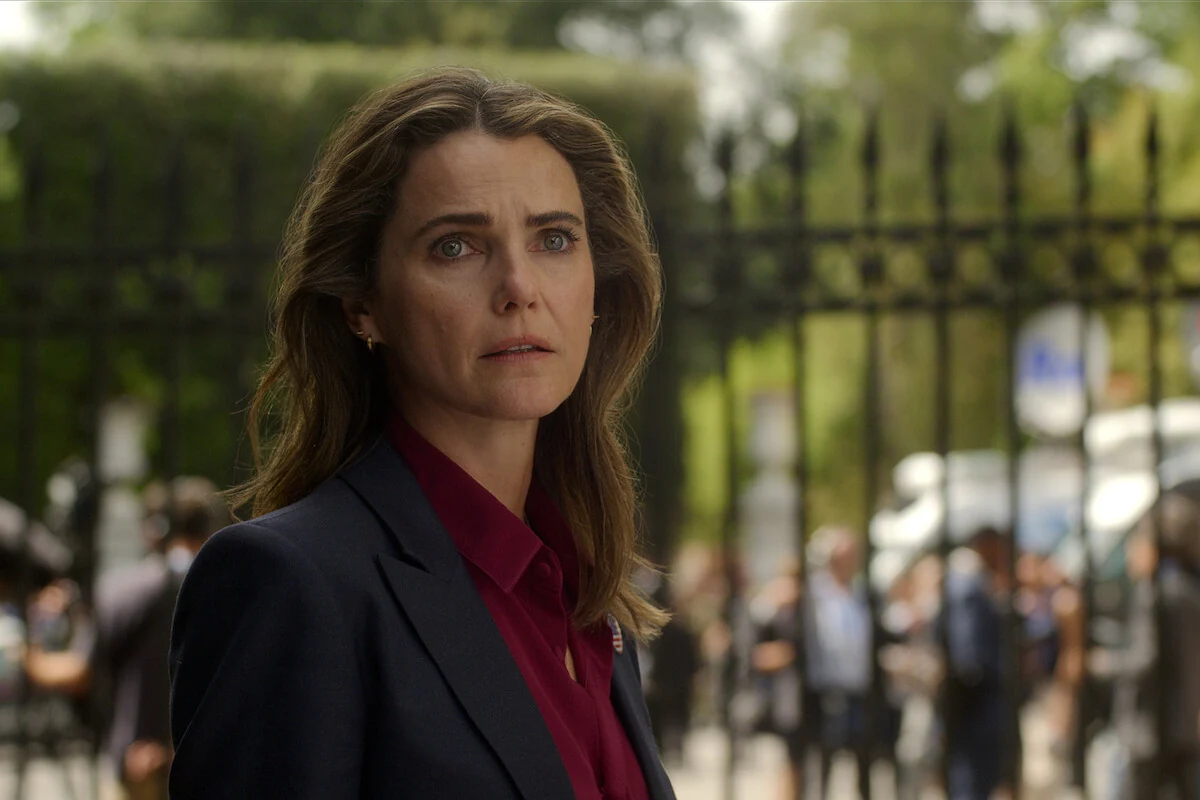 Kate Wyler stands beside an iron fence in a dark jacket and burgundy shirt