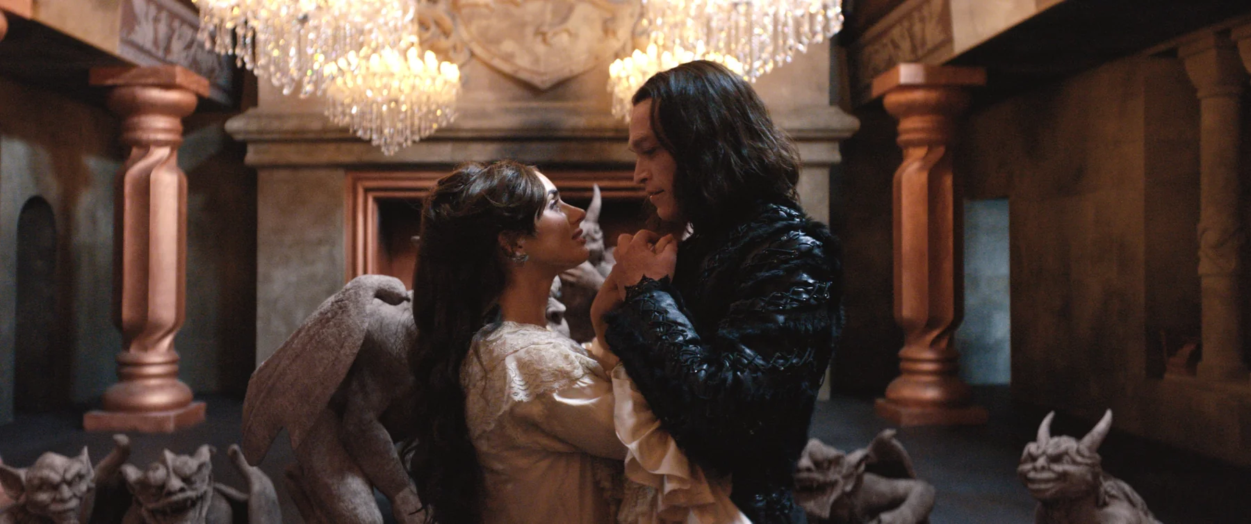 A couple holds hands beneath chandeliers, surrounded by stone creatures in Dracula.