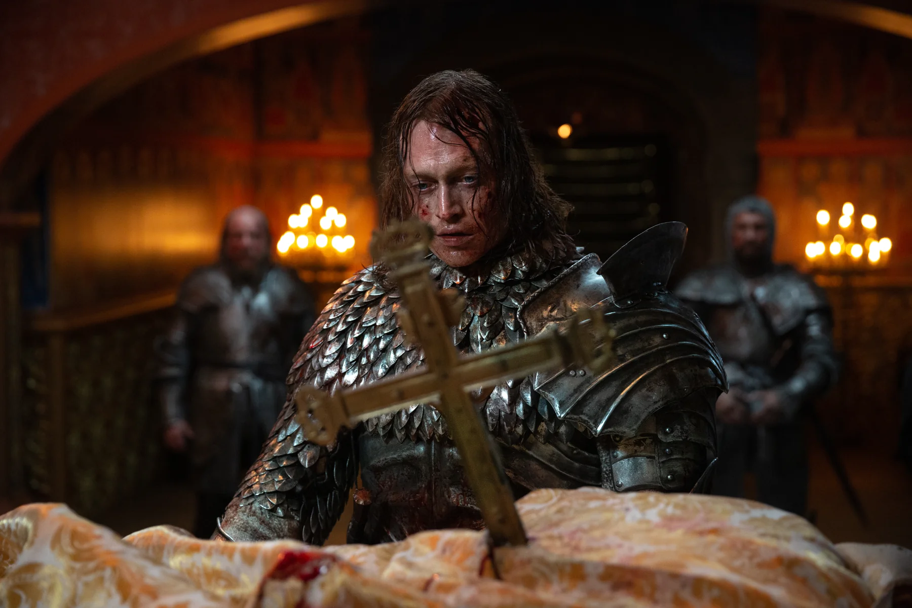 An armored man stands behind a large cross in a candlelit room in Dracula.