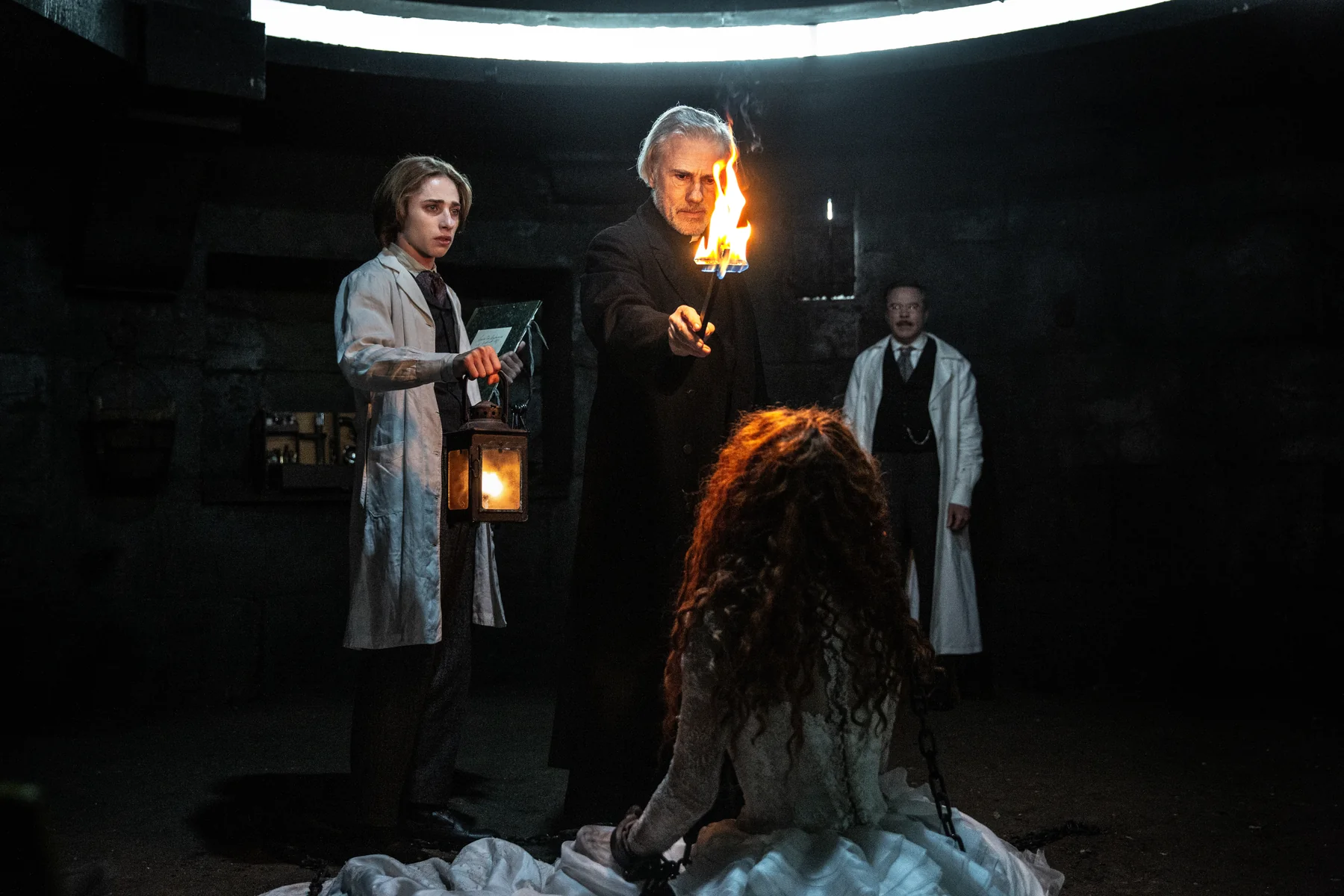 A priest holds a flame toward a seated woman while two men watch in Dracula.