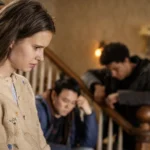 Sara stands beside the staircase with Kenny and Ellis behind her in FROM.