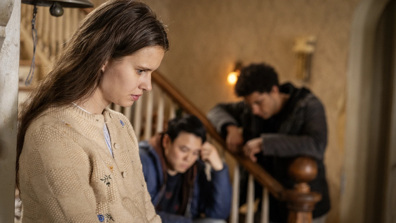 Sara stands beside the staircase with Kenny and Ellis behind her in FROM.