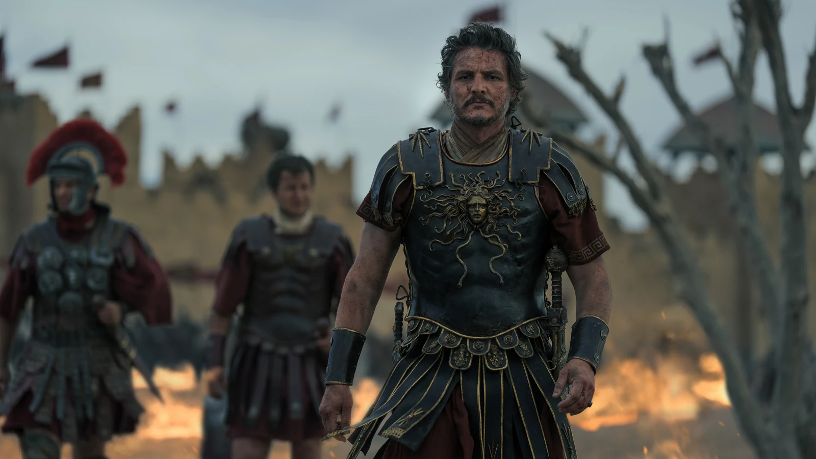 General Acacius stands in armor with soldiers and flames behind him in Gladiator II.