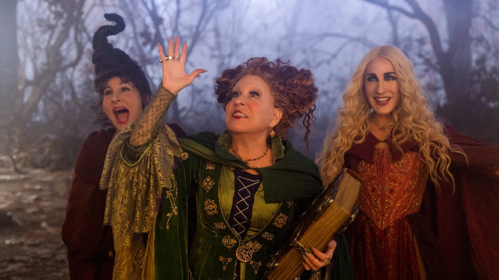 Winifred raises one hand while holding Book between Mary and Sarah in Hocus Pocus 2