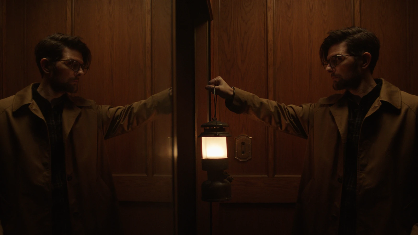 Ohm Bauman holds a lantern beside his reflection in a mirror in Hokum.