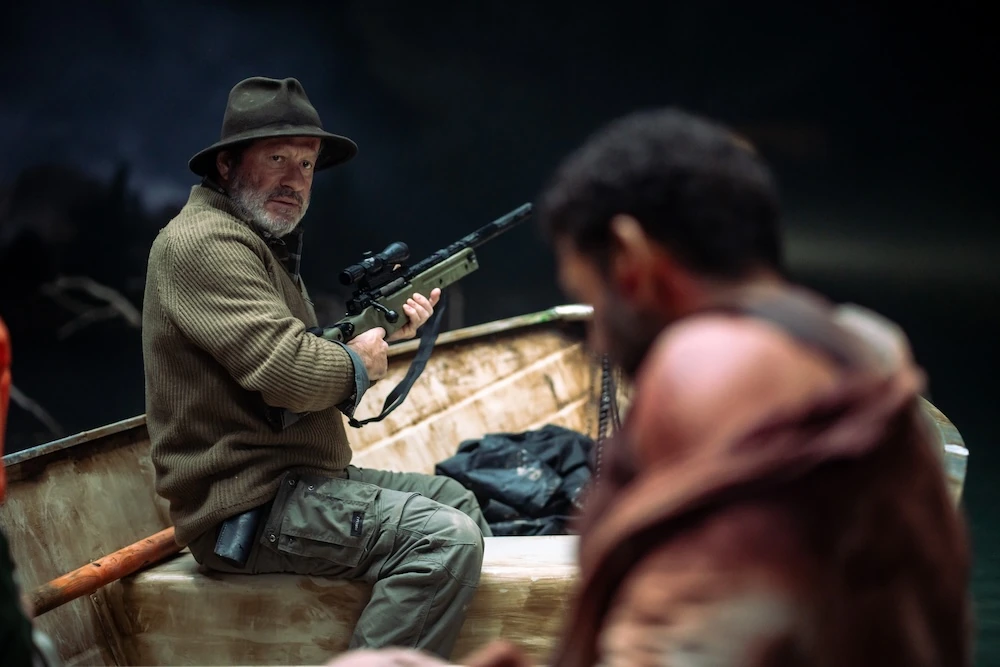 Walker holds a tranquilizer rifle aboard a boat beside another passenger in Hungry.
