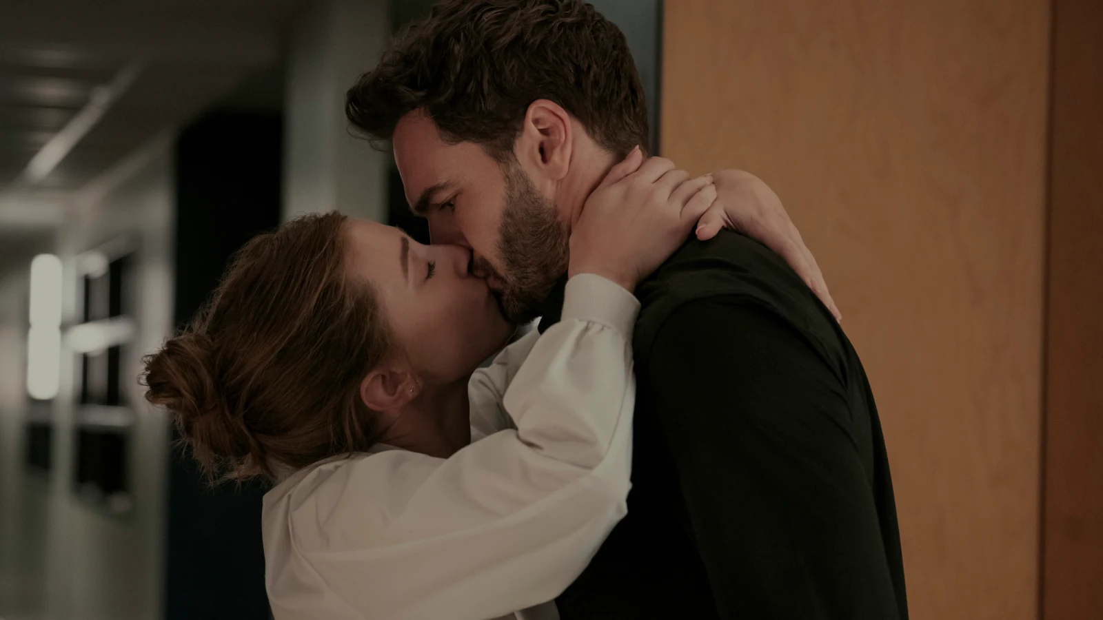 Olive wraps her arms around Adam as they kiss in a hallway.