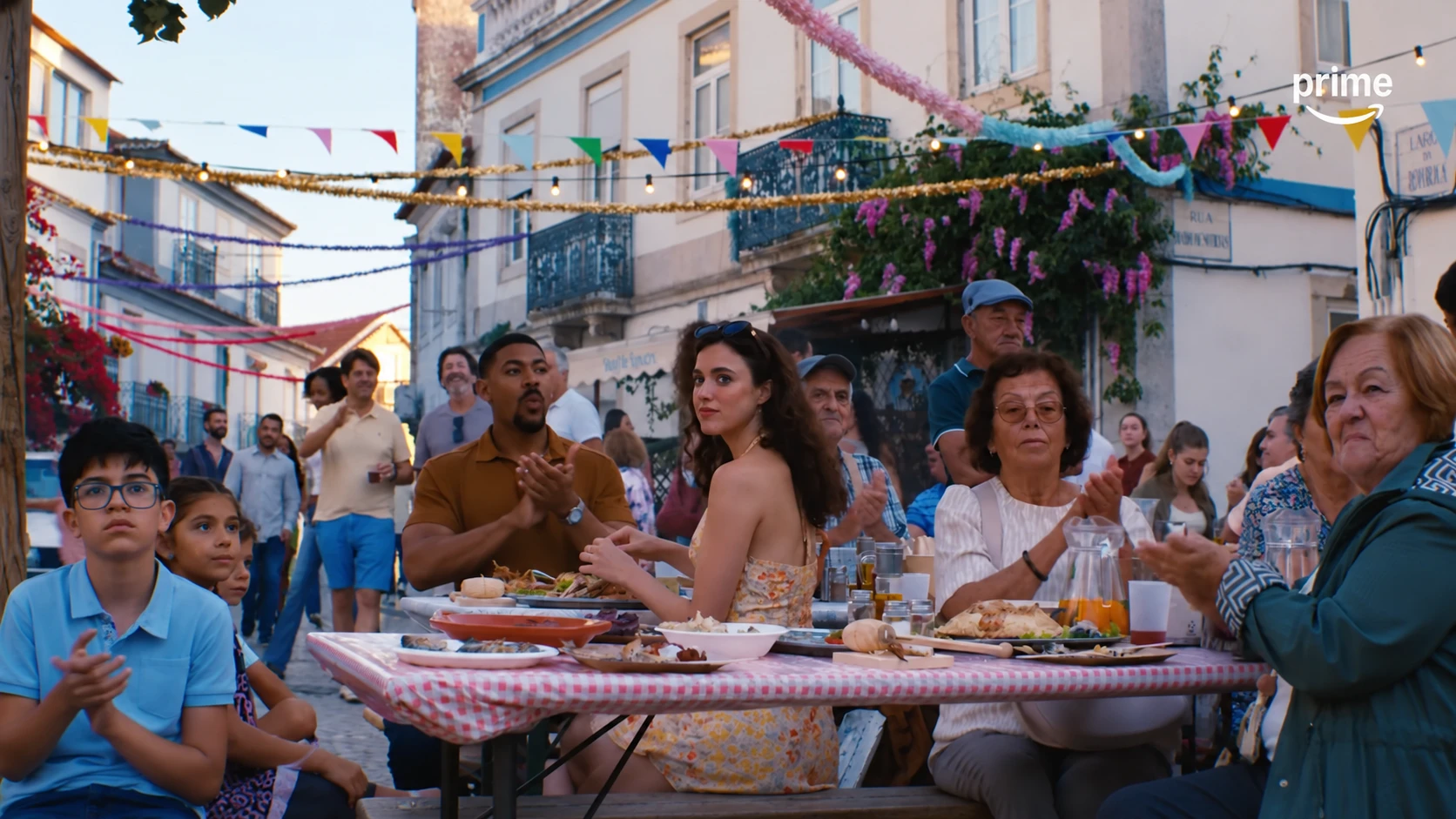 Maya sits among diners at an outdoor meal beneath colorful decorations