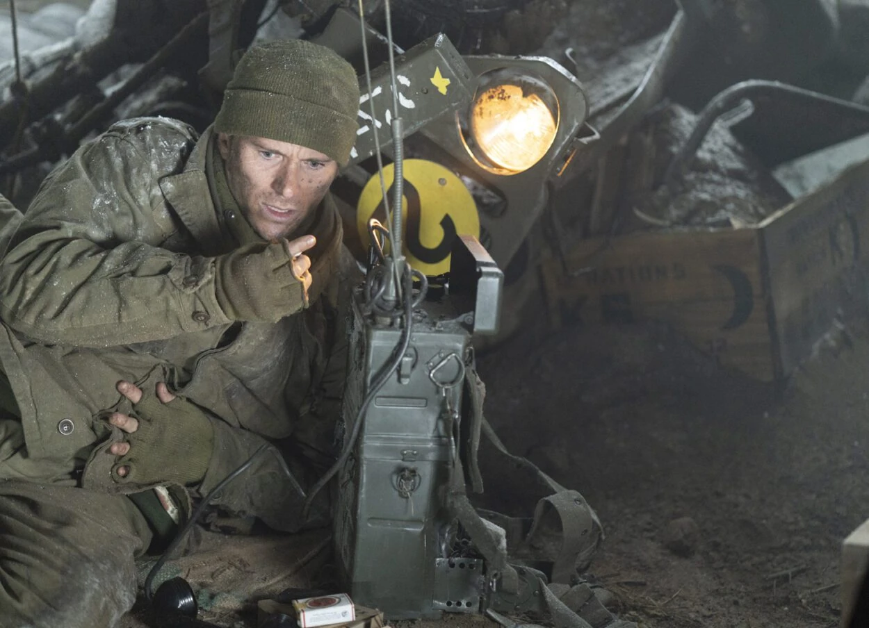 John Castle (Scott Eastwood) crouches beside a field radio and a vehicle headlight in Lucky Strike.