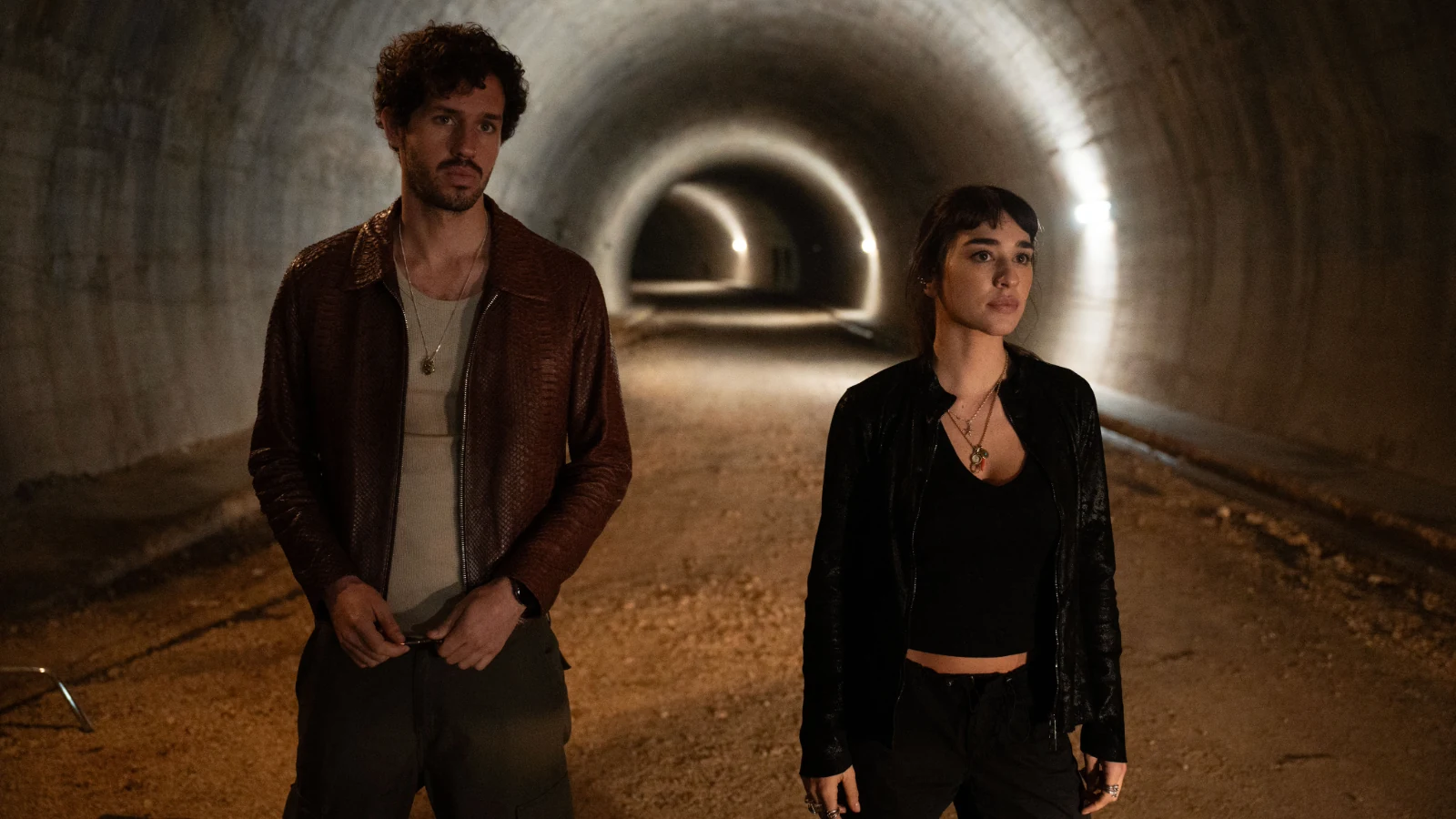 Victor Belmondo and Simona Tabasco stand side by side in a lit tunnel in Masterplan.