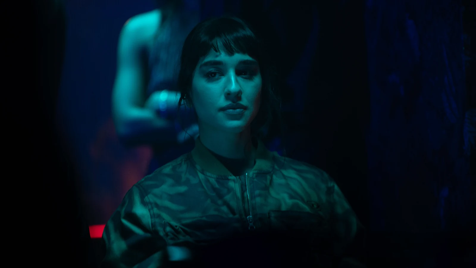 Simona Tabasco wears a zip-front jacket in a close-up lit with blue and teal light.
