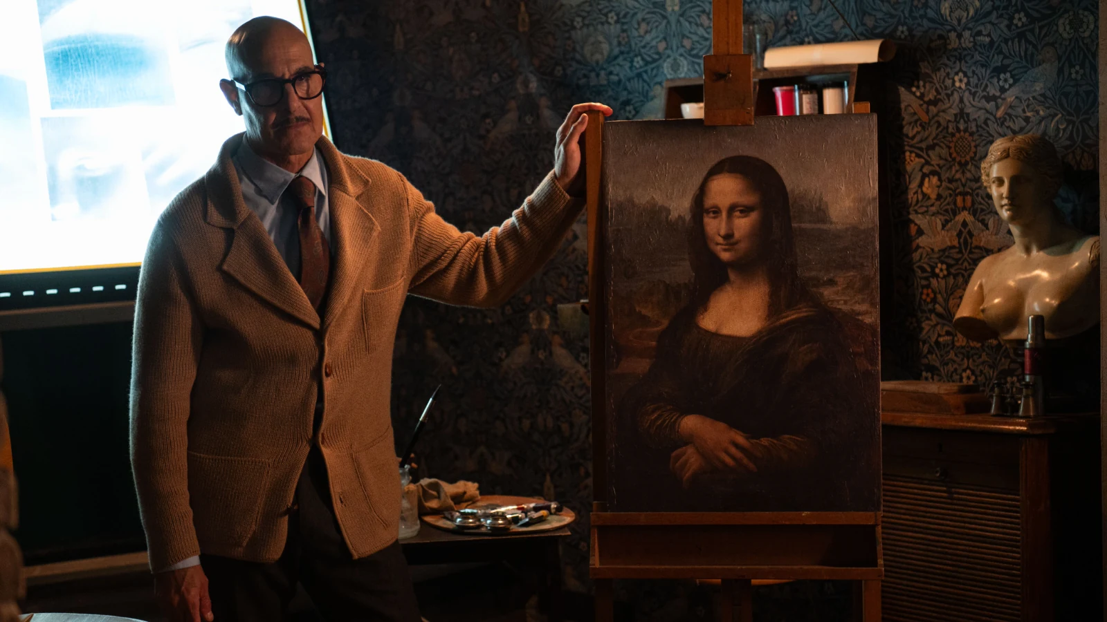 Stanley Tucci stands beside a Mona Lisa painting in Masterplan.