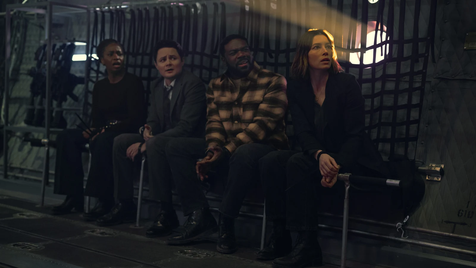 Charmaine, Ted, Crosby, and Aimee sit side by side with their wrists restrained inside an aircraft.