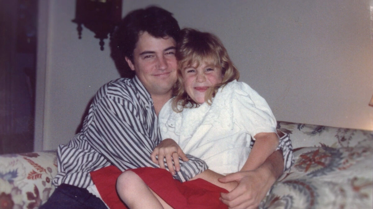 Matthew Perry sits on a floral sofa with a young girl in a family photograph.