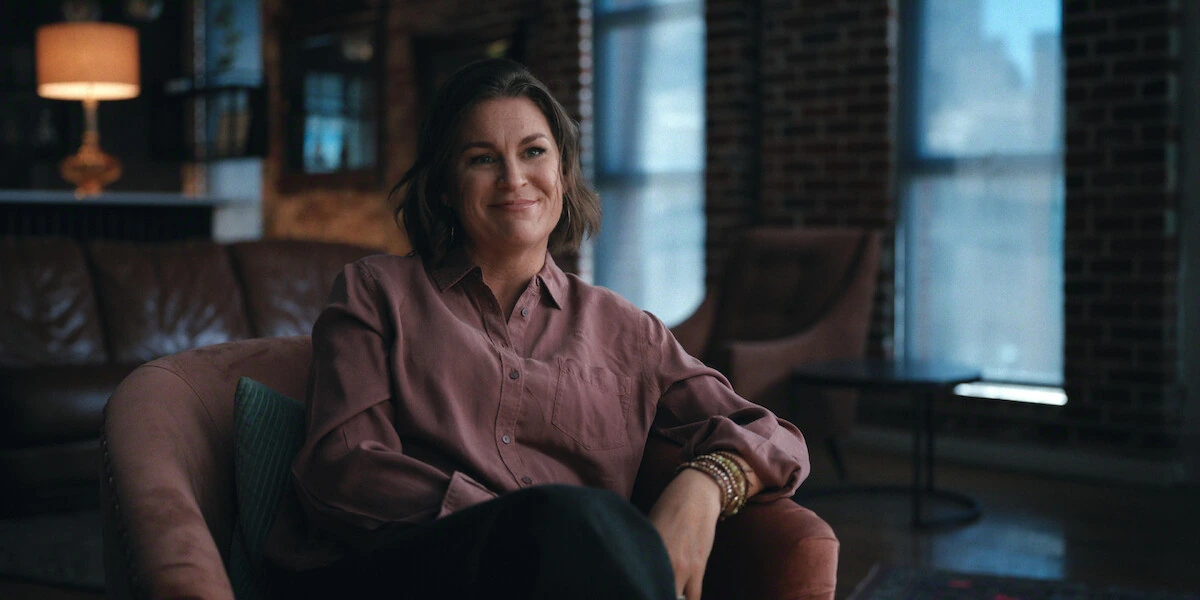 A woman in a mauve shirt sits in an armchair during an interview in The One About Matthew Perry.