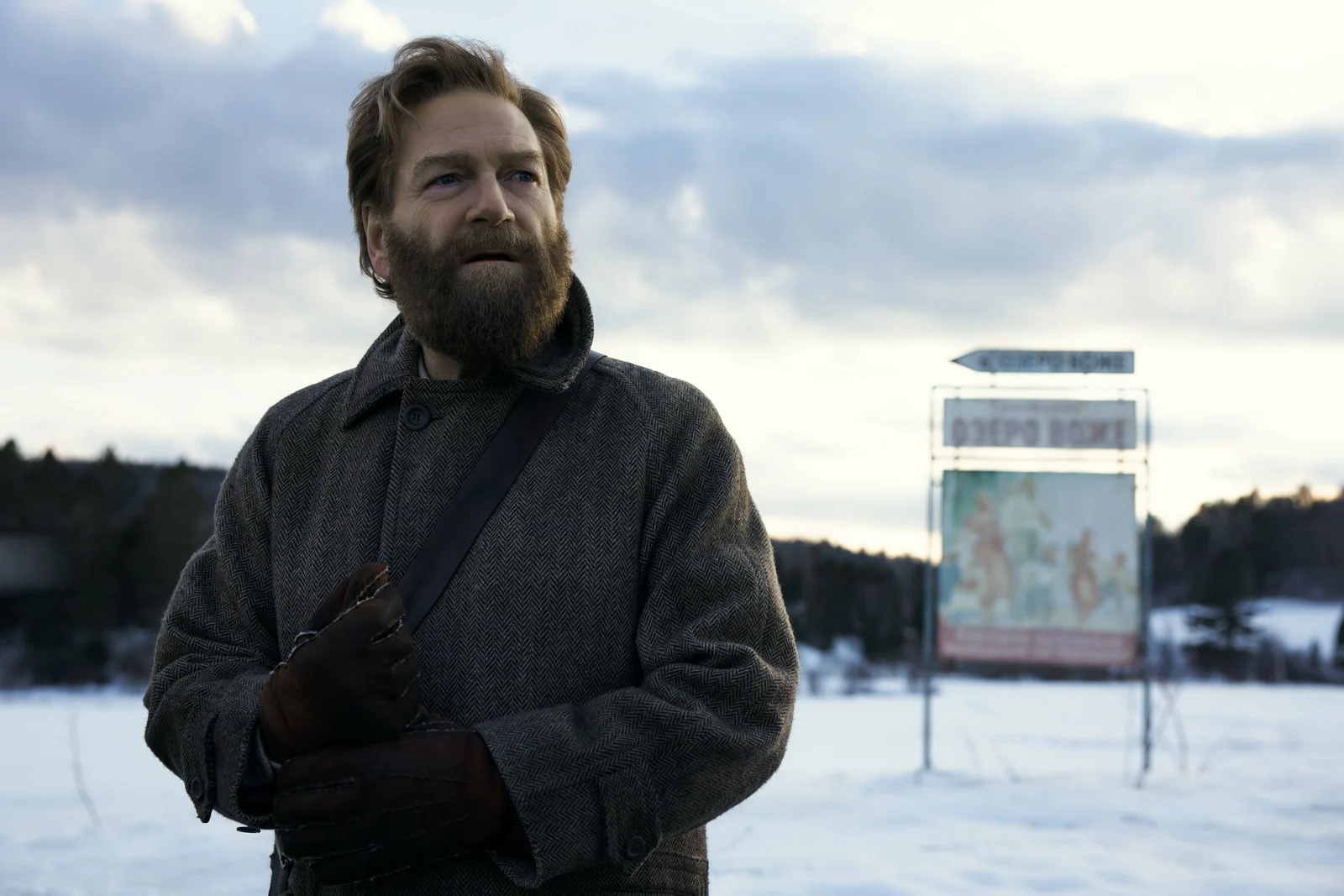 Nikolai wears a gray coat and leather gloves beside a snowy roadside.