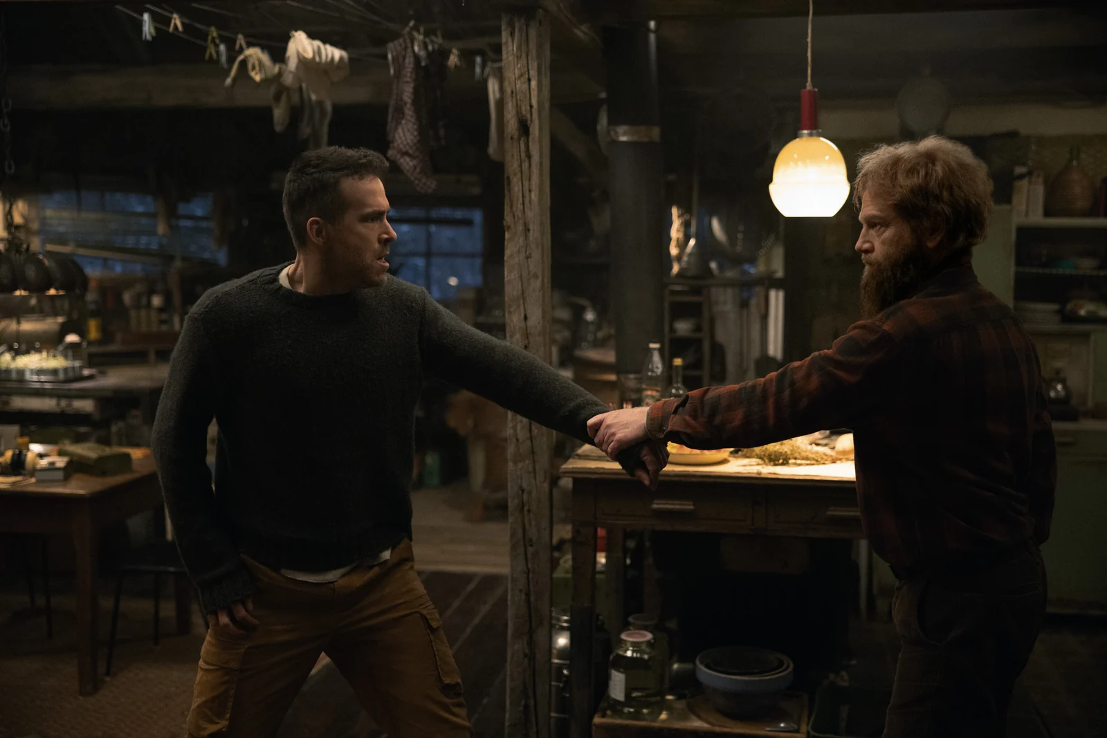 Nikolai grips Troy’s wrist inside a wooden cabin.