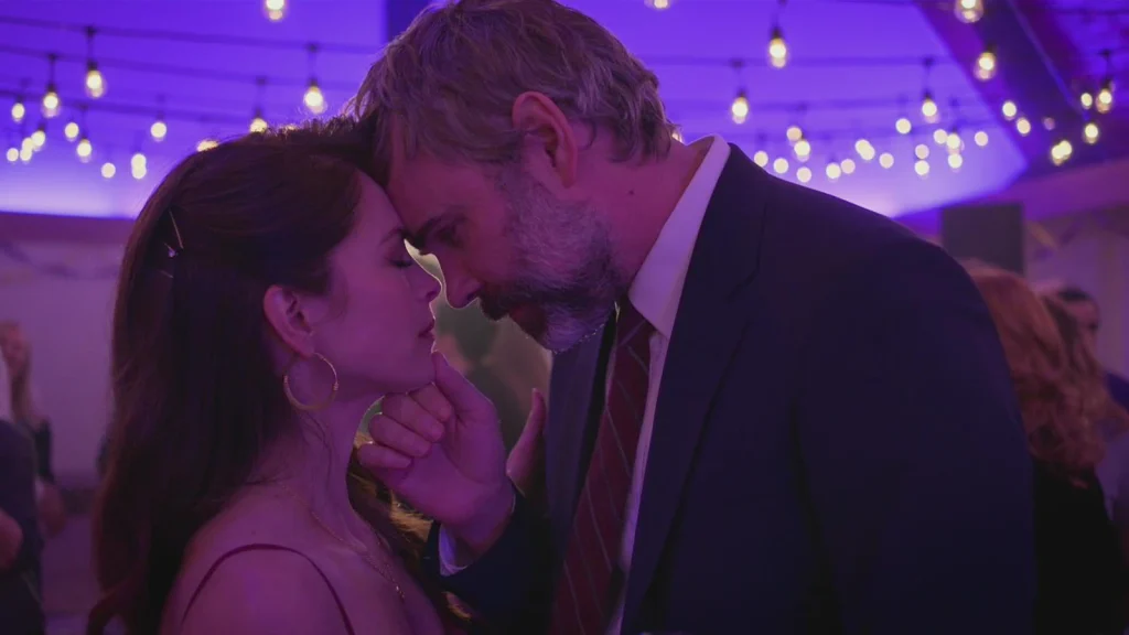 A man and woman lean their foreheads together under purple lights in Murder in a Small Town