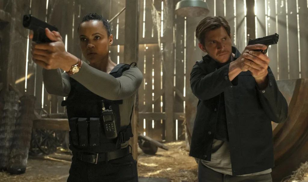 Frances Neagley and Hudson Riley aim their handguns in different directions inside a wooden building. 