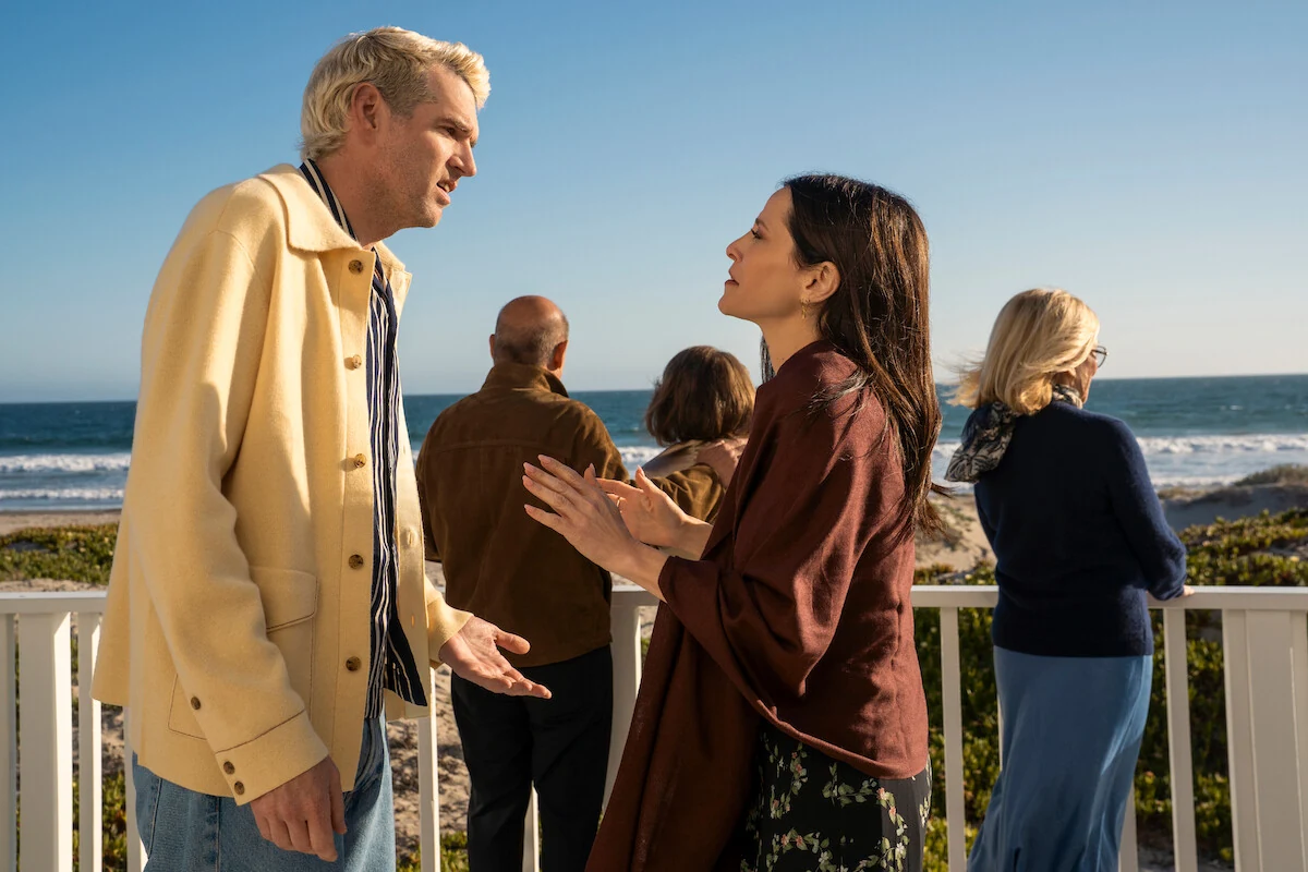 Sasha and Esther face each other on a deck overlooking the ocean.