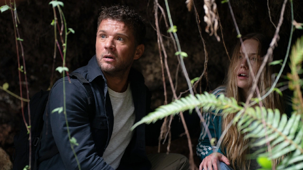 Danny and Alex crouch behind ferns and hanging roots in One Mile.