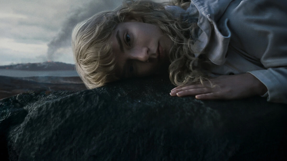 Joan rests her head and hand on a dark rock in Sacrifice