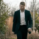 Slow Horses Season 6 Ending: Why River Lets His Father Walk Away Jack Lowden as River Cartwright walks outdoors in a dark suit with a bandaged hand.