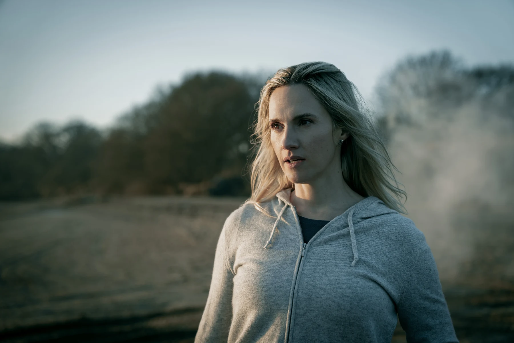Ruth Bradley as Emma Flyte stands outdoors in a gray zip-up hoodie.