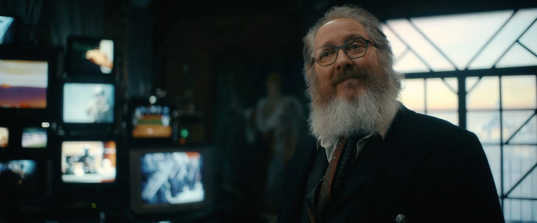 James Spader as Ultron in human form, wearing glasses beside television screens