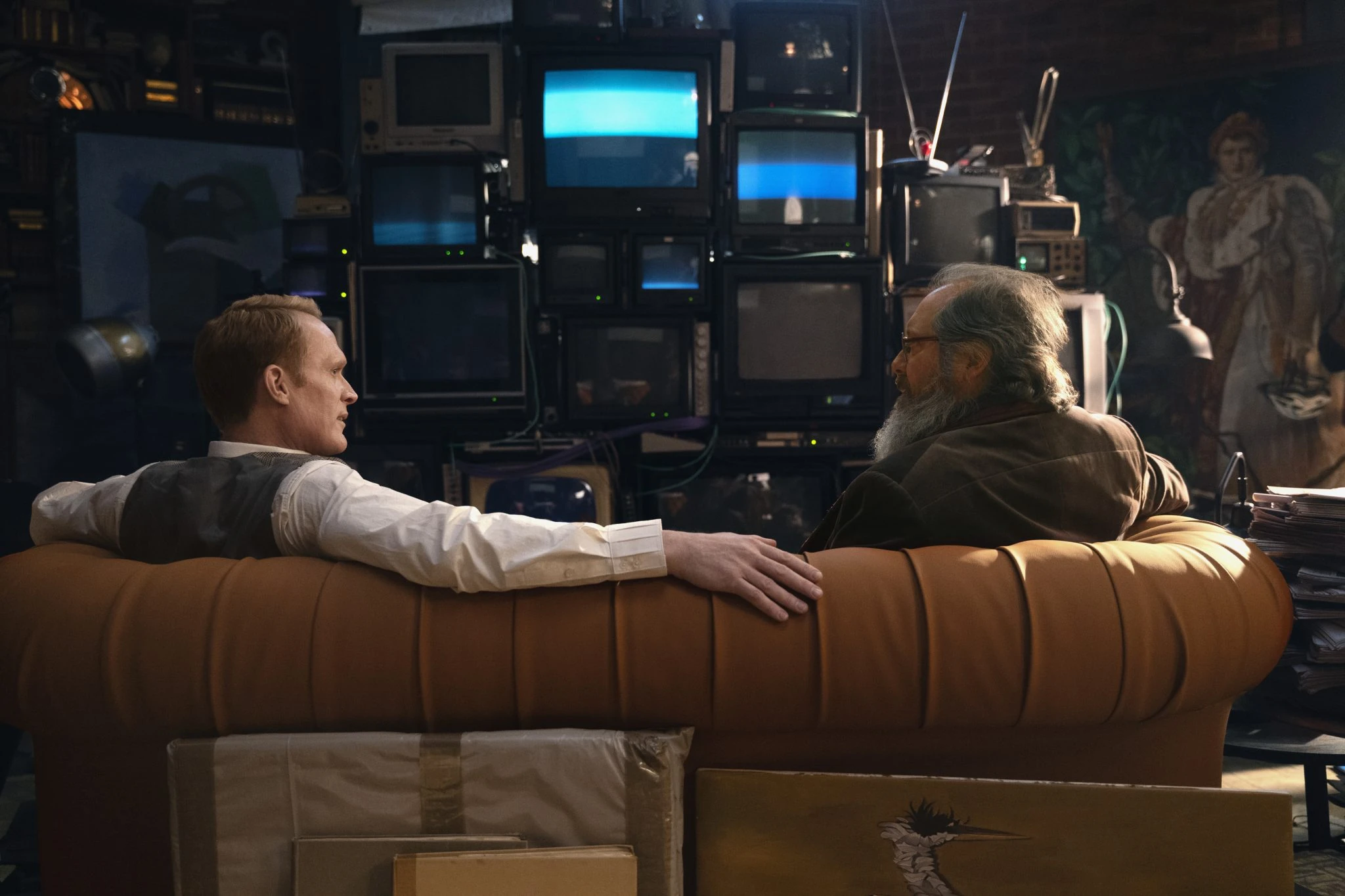 Vision and Ultron sit on a tan sofa facing a wall of televisions