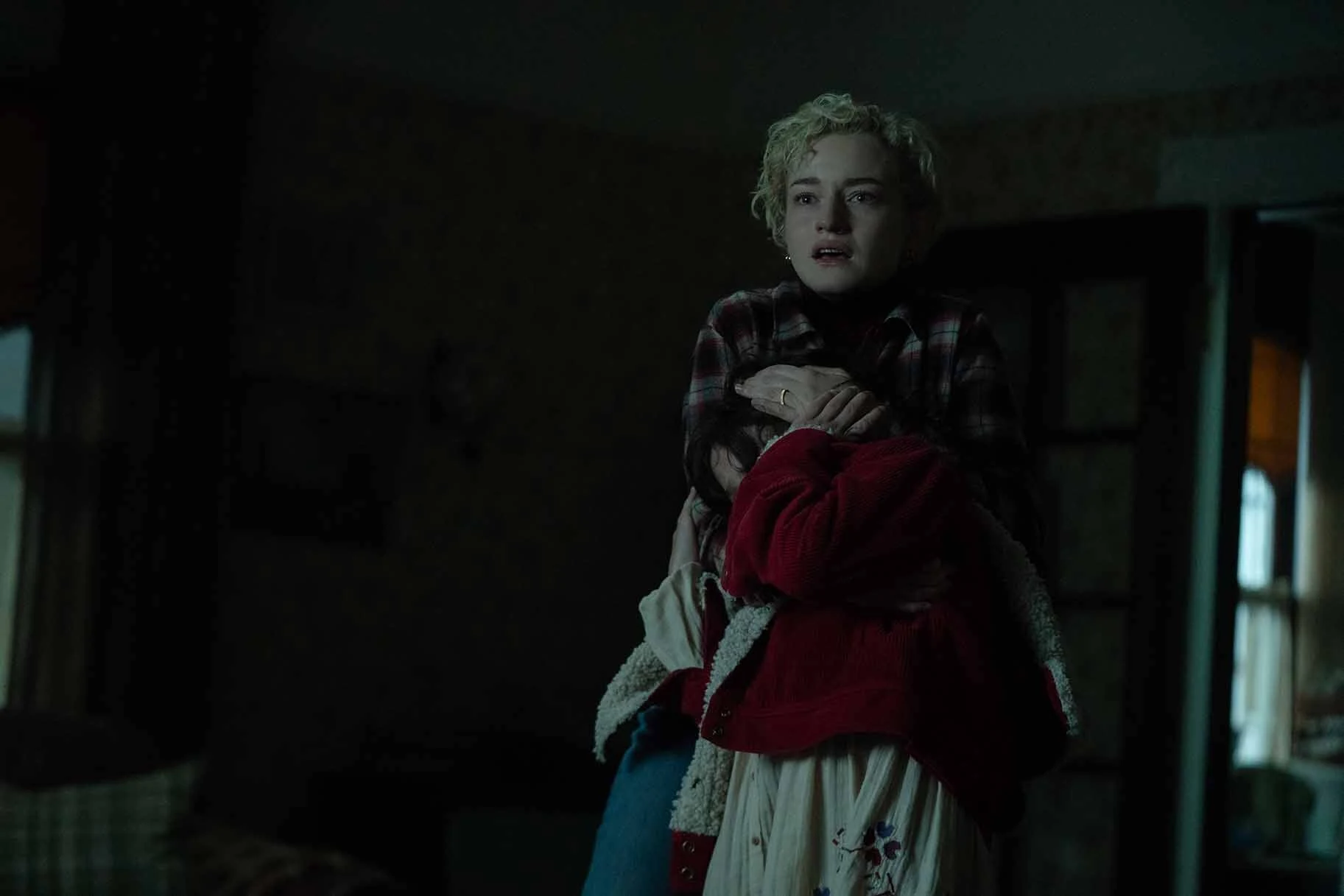 Charlotte wraps her arms around Ginger, who covers her face, in a dim room in Wolf Man.